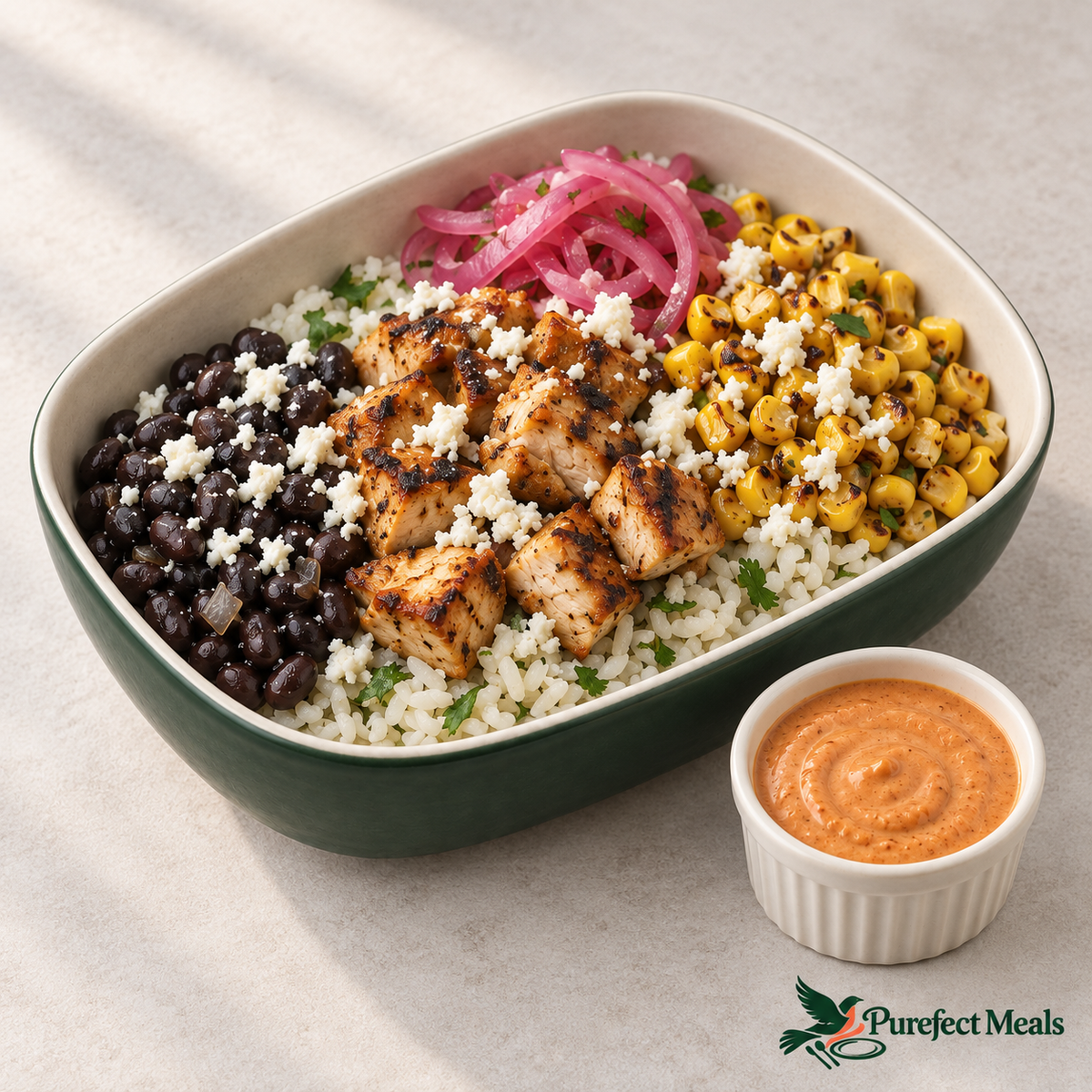 Chipotle chicken burrito bowl with pickled onions, crumbled white cheese, and reddish-orange chipotle lime crema served on the side