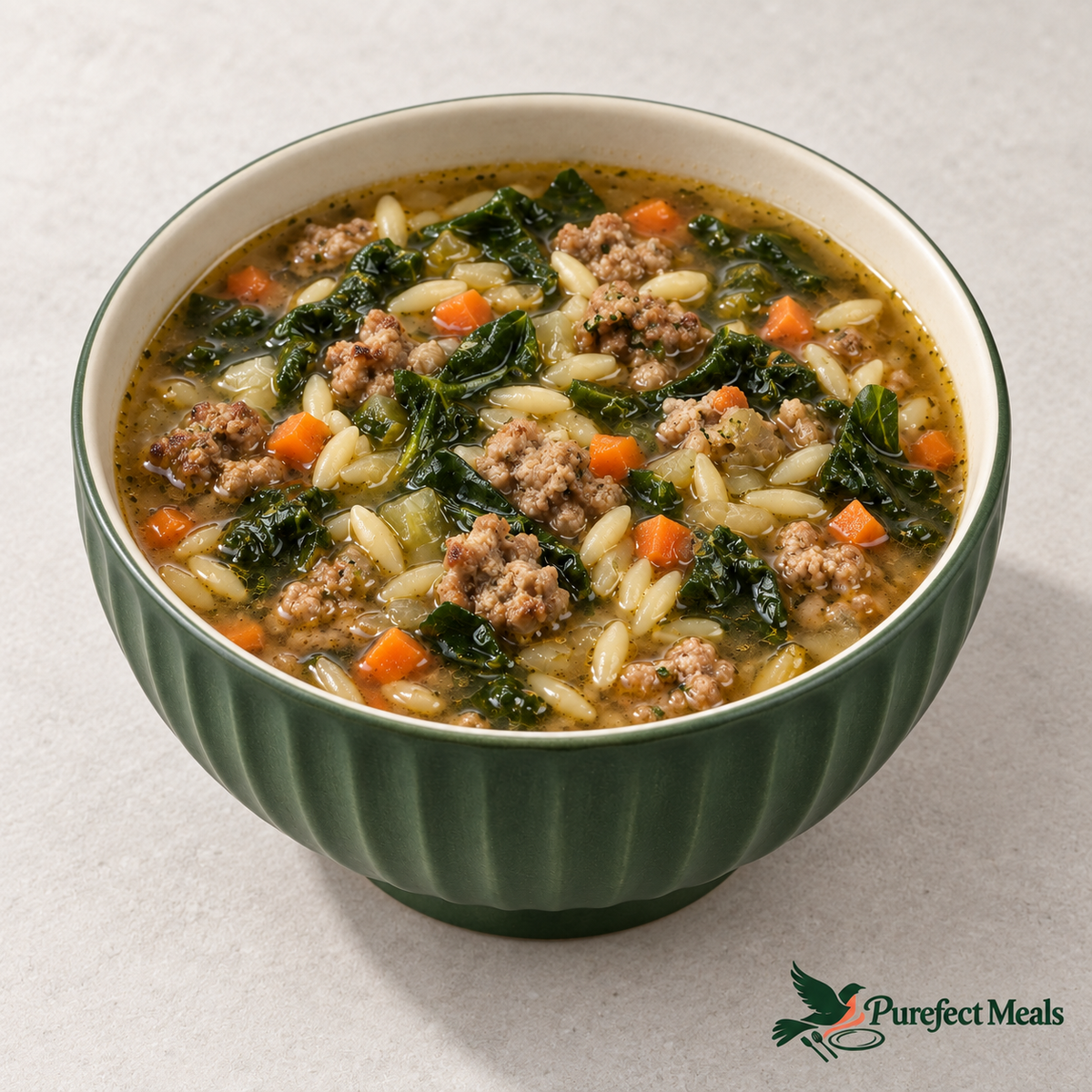 Italian sausage and orzo soup with kale and carrots in a fluted forest-green ceramic bowl on white